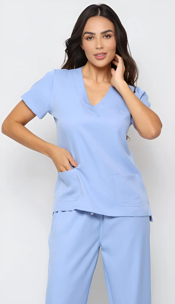 Uma profissional da saúde usando um uniforme médico azul-claro, com uma mão no bolso e a outra tocando o cabelo, exibindo um sorriso confiante e uma postura relaxada. Querendo demonstrar o que é scrub.