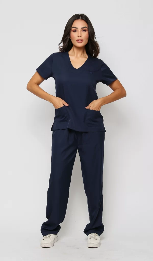 Modelo vestida de scrub/pijama cirúrgico para clínica. O scrub/pijama cirúrgico consiste em uma blusa azul marinho de manga curta com decote em V e dois bolsos frontais, e uma calça combinando. O scrub é ideal para clínica, hospital.